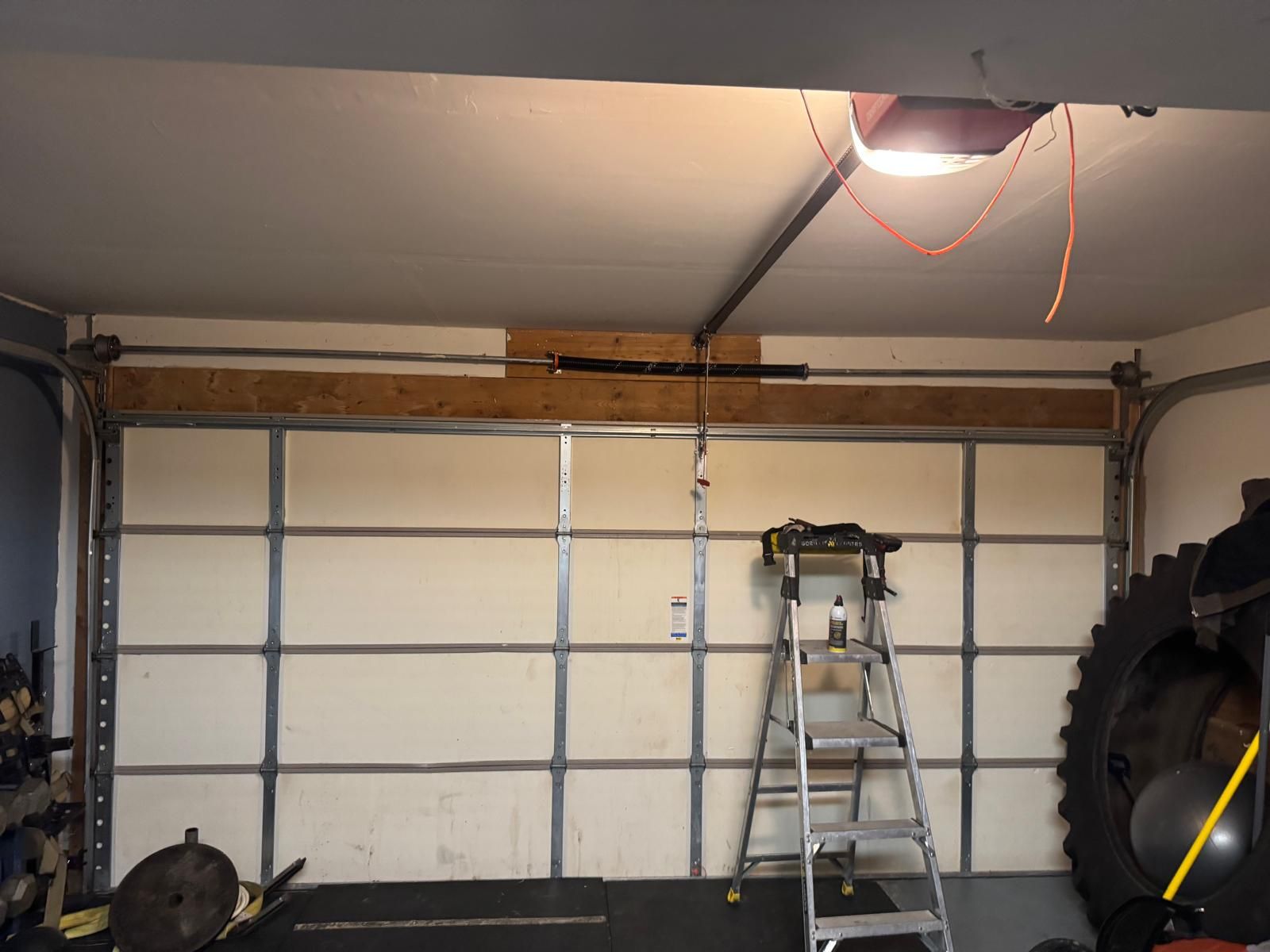 Inside a garage: sectional door, torsion spring above the opening, tracks and ceiling-mounted opener.